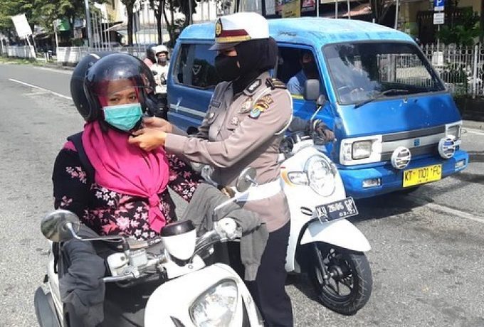 Petugas Satlantas tampak memasangkan tali helm