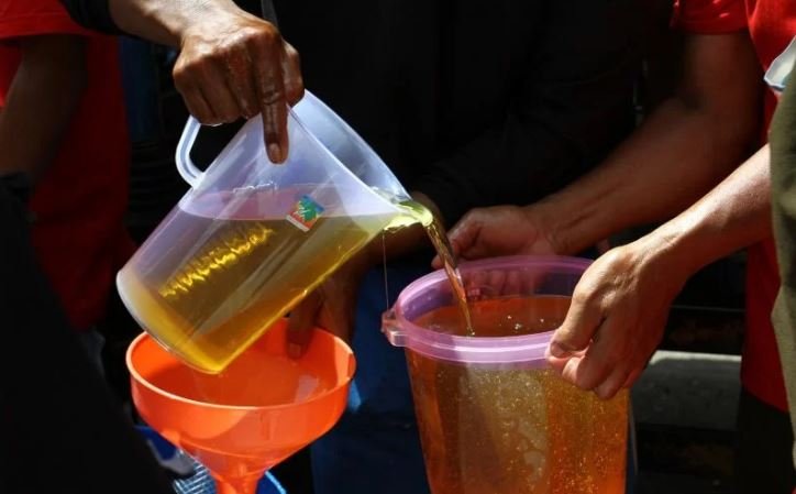 Pekerja menuangkan minyak goreng